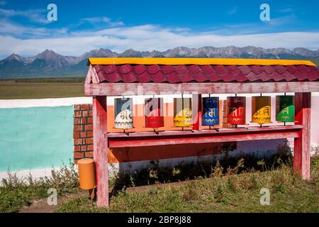 Tibetische Gebetsräder. Buddhistische Spinntrommeln. Mehrfarbige Fässer unter dem Dach. Berge am Horizont. Horizontal. Stockfoto