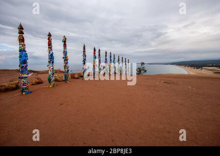 Buddhistische heilige Säulen mit Bändern auf der Insel Olchon am Baikalsee. Viele Säulen in einer Reihe. Der Himmel ist bewölkt. Horizontal. Stockfoto