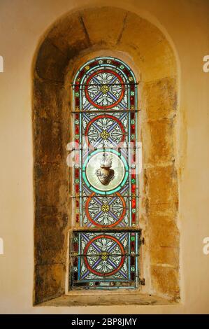 Ein ungewöhnliches Buntglasfenster, das ein in Dornen gehülltes Herz darstellt, in der romanischen Kapelle des Dorfes, eines der schönsten Dörfer in Franc Stockfoto