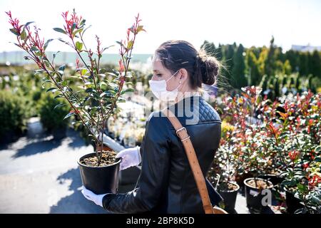 Junge Frau mit Gesichtsmaske im Freien Einkaufen im Garten Zentrum, Corona Virus Konzept. Stockfoto