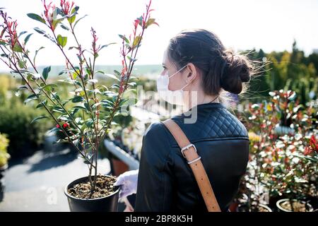 Junge Frau mit Gesichtsmaske im Freien Einkaufen im Garten Zentrum, Corona Virus Konzept. Stockfoto