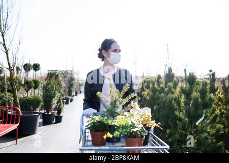 Junge Frau mit Gesichtsmaske im Freien Einkaufen im Garten Zentrum, Corona Virus Konzept. Stockfoto