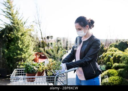 Junge Frau mit Gesichtsmaske im Freien Einkaufen im Garten Zentrum, Corona Virus Konzept. Stockfoto