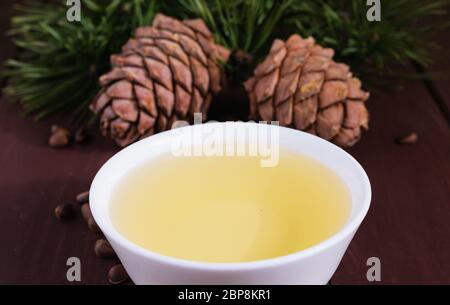 Zedernöl in einer Glasflasche und Zedernkegel mit Nüssen auf einem alten Holztisch. Stockfoto