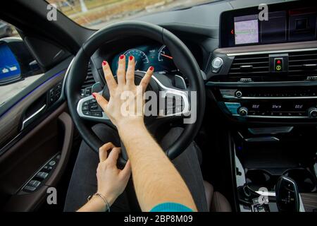 Nervöse Situation auf dem Straßenkonzept. Frau mit der rechten Hand drückt Horn auf das Lenkrad und fährt ein modernes Auto mit schwarzem Interieur Stockfoto
