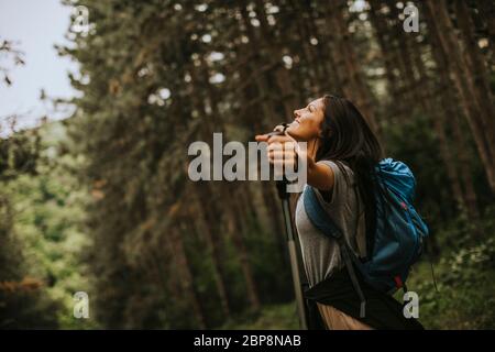 Hübsche junge Frau, die Arme ausbreitet und die Rucksackreise im Wald genießt Stockfoto