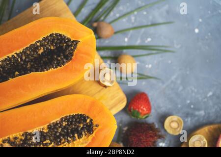 Papaya. Tropische Früchte. Nahaufnahme von zwei Hälften reifer Papaya mit Samen auf Holzschneidebrett. Papaya in Scheiben und andere exotische Früchte auf dem Tisch Stockfoto