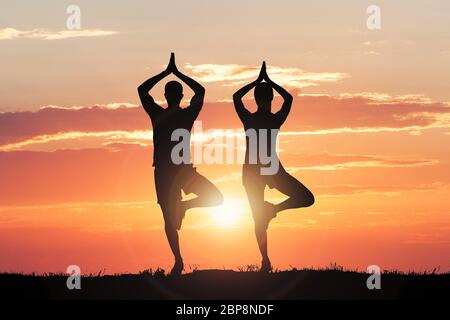 Silhouette von Paar Yoga Gegen dramatische Himmel bei Sonnenuntergang Stockfoto