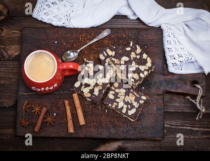 Schwarzer Kaffee mit Schaum in einem roten Keramik Becher auf der Küche Schneidbrett und Schokolade Gebäck mit Mandeln bestreut, Ansicht von oben Stockfoto