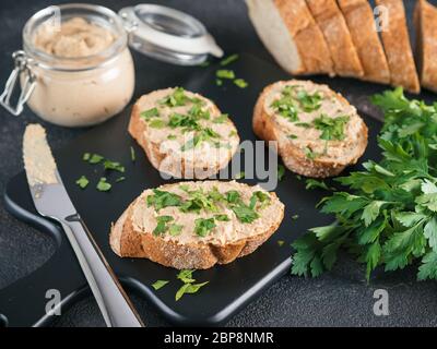 Nahaufnahme der Scheibe Brot mit hausgemachten Türkei Pastete und frische grüne Petersilie auf Schwarz kutting Board über schwarzen Zement Hintergrund, Stockfoto
