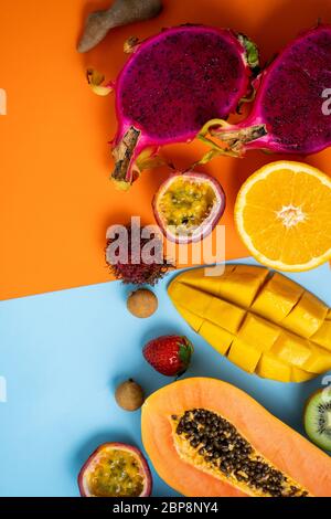 Vertikaler Schuss tropischer Früchte auf orangeblauem Hintergrund. Kreatives Layout aus frischen Papaya, Rambutan, Mango, Passionsfrucht, Orange, Londan, Stra Stockfoto