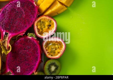 Nahaufnahme von tropischen exotischen Früchten in Scheiben auf dem grünen Schneidebrett. Draufsicht. Platz für Text kopieren. Frische Mango, Drachenfrucht, Kiwi, Maracuja, Pap Stockfoto