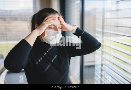 Frau mit Kopfschmerzen und Gesichtsmasken zuhause, Corona Virus Konzept. Stockfoto