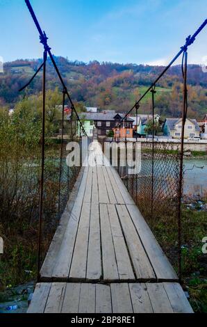Alte Hängebrücke auf zwei Stahlseilen mit Holzboden über den Fluss in einem Bergdorf Stockfoto