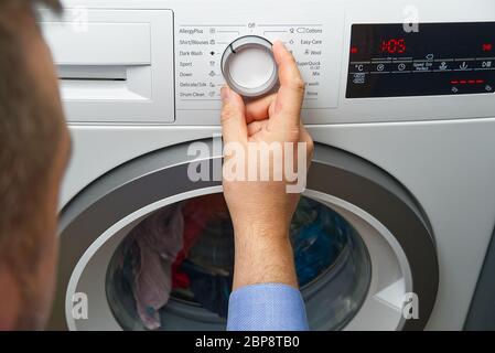 Der Mann stellt das Programm ein und schaltet die Waschmaschine ein. Nahaufnahme der Person, die die Taste der Waschmaschine für die Wäsche drückt Stockfoto
