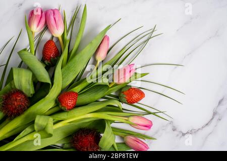 Nahaufnahme eines schönen Blumenstraußes mit roten Erdbeeren auf einem Marmortisch mit Platz für Text. Frühling, Sommer, Tulpen Stockfoto