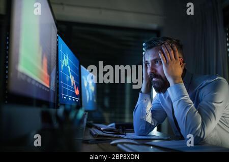 Frustrierter Geschäftsmann mit Computer an der Rezeption, der spät arbeitete. Konzept der Finanzkrise. Stockfoto