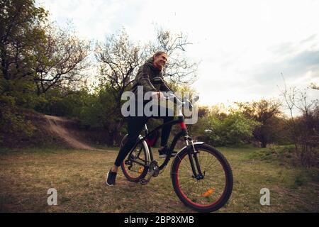 Junger Mann mit Spaß in der Nähe von Landschaftspark, Fahrrad fahren, Reisen im Frühling Tag. Ruhige Natur, Frühlingstag, positive Emotionen. Sportliche, aktive Freizeitaktivitäten. Wandern in Bewegung, blühende Natur. Stockfoto