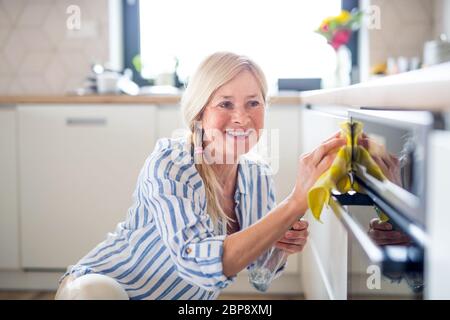 Porträt von älteren Frau Reinigung Ofentür drinnen in der Küche zu Hause. Stockfoto