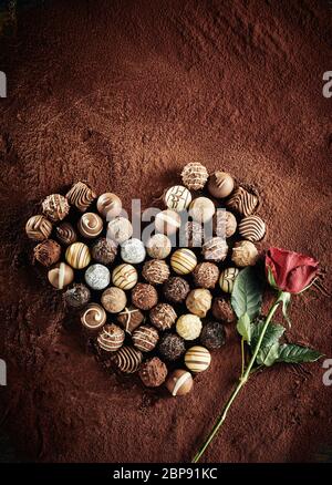 Herz immer noch geprägt von einer sortierten Auswahl luxus Schokolade Bonbons auf einem Bett von Kakaopulver mit einer roten Rose Symbol von Liebe ad Romanze mit Co Stockfoto