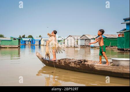 Ein junger kambodschanischer Junge imitiert seinen Bruder, während er sein Fischernetz ins Wasser wirft. Schwimmende Dorf in Kompong Chnnang, Kambodscha, Südostasien Stockfoto