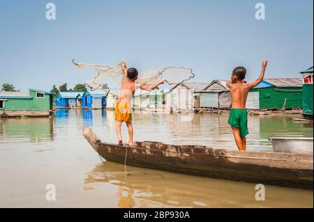 Ein junger kambodschanischer Junge imitiert seinen Bruder, während er sein Fischernetz ins Wasser wirft. Schwimmende Dorf in Kompong Chnnang, Kambodscha, Südostasien Stockfoto