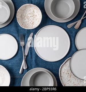 Leere keramisches Geschirr. Keramikplatten auf Jeans Tischdecke oder Läufer. Übersicht leere Tabelle mit Geschirr. Satz von verschiedenen modernen weißen Platten Stockfoto