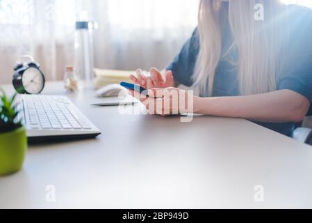 Junge Frau sitzt an einem Schreibtisch und tickt auf dem Smartphone Stockfoto