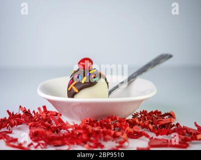 Banana Split weißen Kuchen Pop Ball mit Schokolade beträufelt darüber und streut mit einer Kirsche auf der Oberseite sitzt in einer weißen Keramikschale auf rotem pape Stockfoto