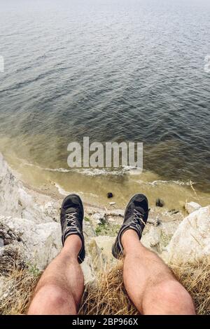 POV-Sicht der Mann sitzt auf dem Rand der Klippe mit Blick auf den Fluss Stockfoto