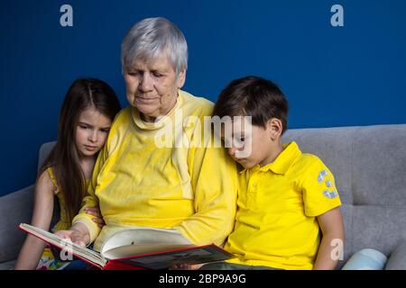 Eine alte Großmutter und ihre geliebten Enkelkinder sitzen zu Hause und lesen ein Interessantes Buch Stockfoto