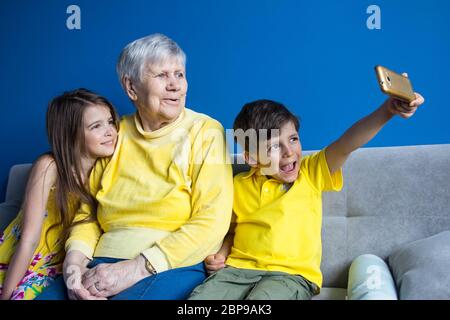 Eine alte Großmutter und ihre geliebten Enkelkinder sitzen zu Hause und fotografieren auf ihrem Smartphone Stockfoto