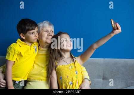 Eine alte Großmutter und ihre geliebten Enkelkinder sitzen zu Hause und fotografieren auf ihrem Smartphone Stockfoto