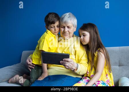 Eine alte Großmutter und ihre geliebten Enkelkinder sitzen zu Hause und telefonieren Stockfoto