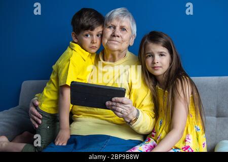 Eine alte Großmutter und ihre geliebten Enkelkinder sitzen zu Hause und telefonieren Stockfoto