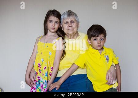 Eine alte Großmutter und ihre geliebten Enkelkinder sitzen zu Hause und umarmen sich Stockfoto