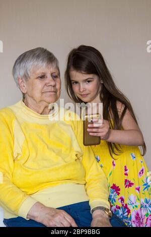 Eine alte Großmutter und ihre geliebten Enkelkinder sitzen zu Hause und telefonieren Stockfoto