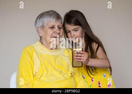 Eine alte Großmutter und ihre geliebten Enkelkinder sitzen zu Hause und telefonieren Stockfoto