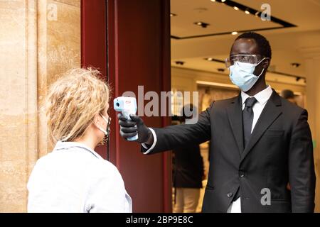 Ein Mann, der eine Gesichtsmaske als vorbeugende Maßnahme trägt, überprüft die Körpertemperatur einer Frau, bevor er in ein Gebäude eintritt.die zweite Phase der Behandlung von Coronavirus beginnt in Italien mit der Eröffnung von Geschäften und Kirchen. Italien hat bisher 225,675 Fälle von Coronavirus, 32,053 Todesfälle und 125 000 Genesen bestätigt. Stockfoto