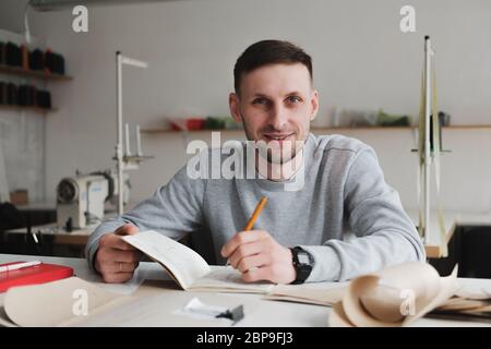 Lächelnder Mann, der in einer generischen Werkstatt Ingenieursarbeit oder Managementarbeit leistet. Lokale Kleinunternehmen, Kleidung Designer Porträt Stockfoto