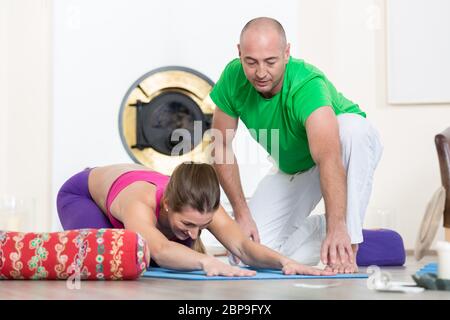 Männliche Ausbilder helfen jungen weiblichen Studenten zu tun Yoga Pose Stockfoto