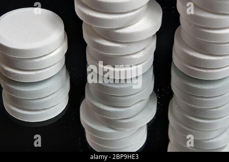 Pillen auf einer Spiegelfläche mit schwarzem Hintergrund gestapelt. Gesundheits- und medizinische Themen Stockfoto