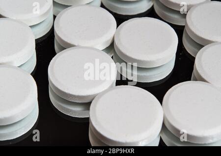 Pillen auf einer Spiegelfläche mit schwarzem Hintergrund gestapelt. Gesundheits- und medizinische Themen Stockfoto