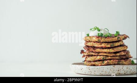 Gluten frei Zucchini Fritten in Stapel auf weißem Hintergrund. Zucchini Pfannkuchen oder Fritten mit grünen Zwiebeln und Parmesan-Käse, serviert saure Sahne oder g Stockfoto