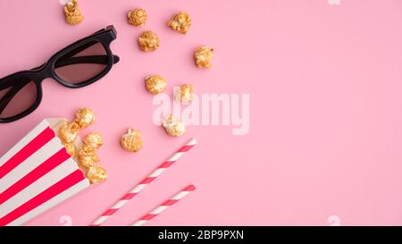 Pop Mais in gestreiften rot-weißen Karton-Box, 3d-Gläser, trinken Strohhalme auf rosa Tischansicht. Online-Kino, Filmkonzept ansehen. Stockfoto