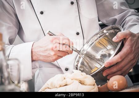 Kaukasischer Männlicher Chef Mischer Teig Mit Drahtbesen In Edelstahl Schüssel. Stockfoto