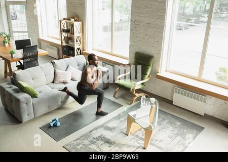 Junger afroamerikanischer Mann trainiert zu Hause während der Quarantäne des Coronavirus Ausbruch, doinc Übungen der Fitness, Aerobic. Sportivfähigkeit während der Isolierung. Wellness, Bewegungskonzept. Sit ups. Stockfoto