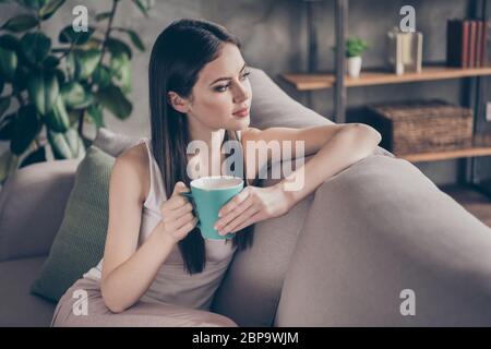 Profil Seite Foto von ruhigen ruhigen ruhigen Mädchen sitzen Divan Blick halten leckere Kaffee Tasse Traum Plan grübeln das Leben im Wohnzimmer Innenhaus im Haus Stockfoto