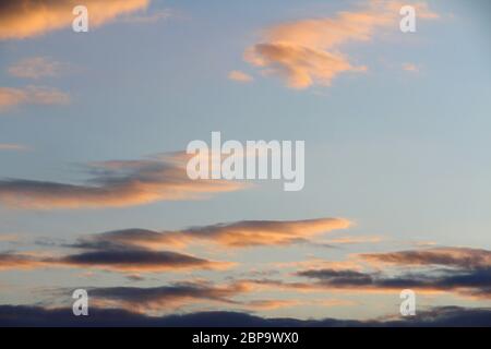 Wolken am Himmel werden von unten durch das rote Licht der Sonne beleuchtet. Sonnenuntergang oder Sonnenaufgang in der Dämmerung. Stockfoto