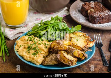 Knusprige zerschlagen Kartoffeln, Rührei und kleinen Salat, Saft und Kuchen zum Frühstück Stockfoto